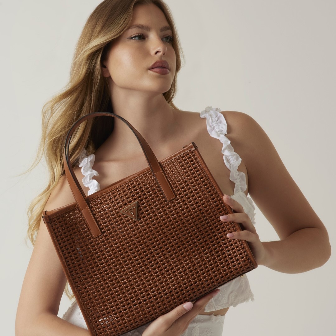 a model holding a brown woven handbag from GUESS